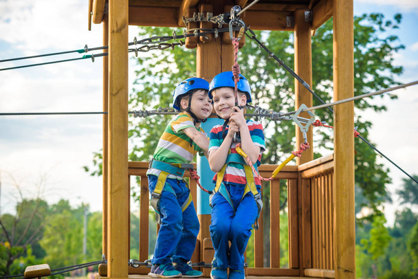 Šťastné děti baví v parku dobrodružství. Dva dobrodružné zdravá školka chlapci, dvojčata těší aktivní den venku lezení na stromy. Koncept přátelství a bratrství. - Fotografie, Obrázek