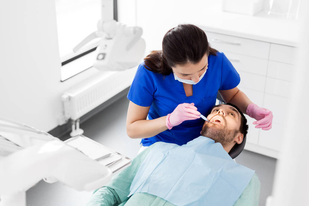female dentist checking up male patient teeth - Fotó, kép