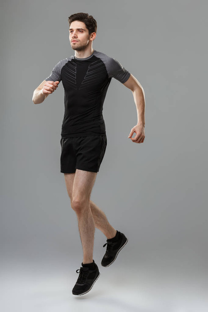 Full length portrait of a concentrated young sportsman warming up isolated over gray background - Foto, afbeelding