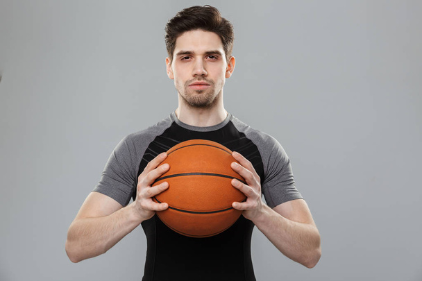 Portrait of a concentrated young sportsman with a basketball isolated over gray background - Fotó, kép