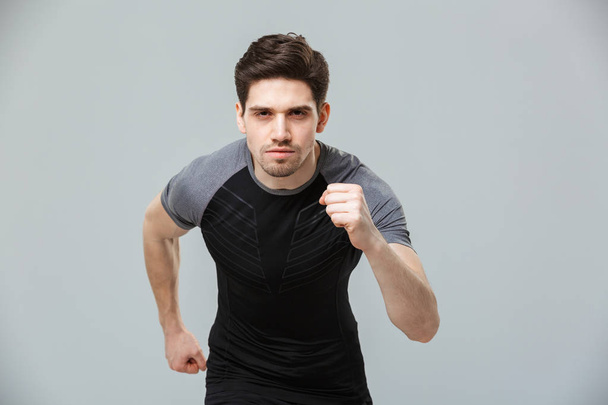 Portrait of a concentrated young sportsman ready to run isolated over gray background - Foto, imagen