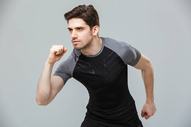 Portrait of a serious young sportsman ready to run isolated over gray background - Foto, Imagem