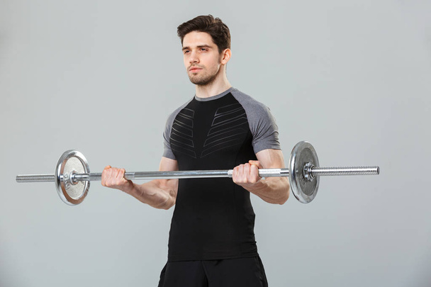 Portrait of a focused young sportsman lifting heavy barbell isolated over gray background - Fotografie, Obrázek