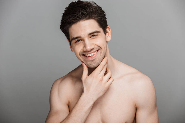 Beauty portrait of half naked laughing young man looking at camera isolated over gray background - Fotoğraf, Görsel