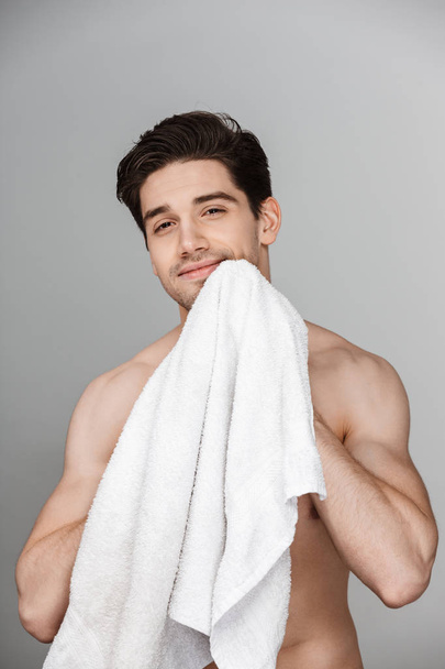 Beauty portrait of half naked handsome young man using a towel isolated over gray background - 写真・画像