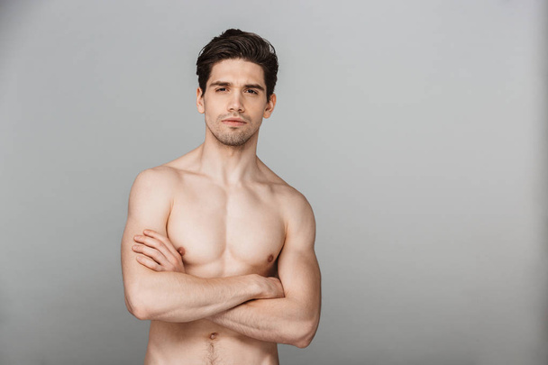 Beauty portrait of half naked confident young man looking at camera with arms folded isolated over gray background - Foto, immagini