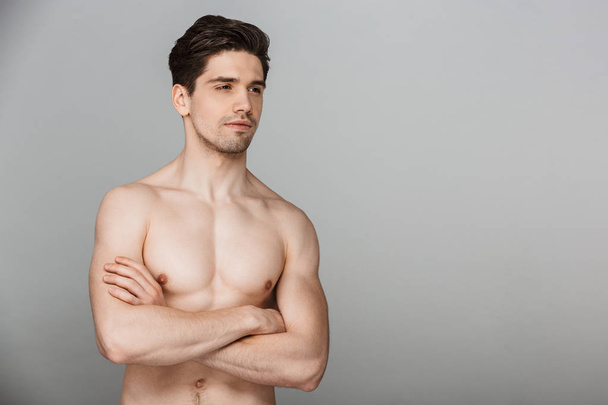 Beauty portrait of half naked confident young man looking away with arms folded isolated over gray background - Foto, Imagem