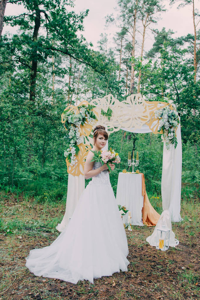 Hermosa mujer en un vestido de novia en una fotozona decorada con flores frescas, posando y retrato
. - Foto, imagen
