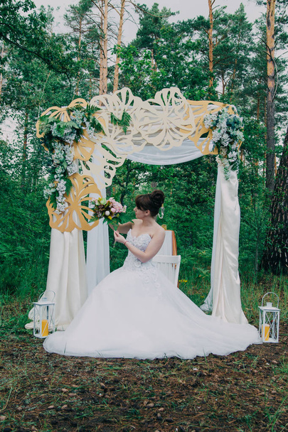 Hermosa mujer en un vestido de novia en una fotozona decorada con flores frescas, posando y retrato
. - Foto, imagen