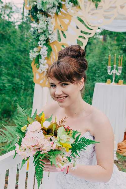 Kaunis nainen hääpuku fotozone koristeltu tuoreita kukkia, poseeraa ja muotokuva
. - Valokuva, kuva