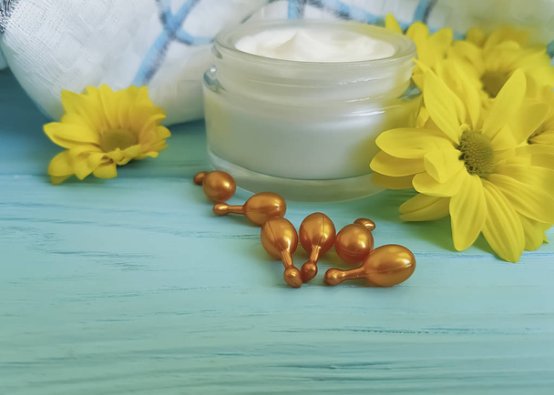 crème cosmetische capsule gele bloemen op een blauwe houten achtergrond - Foto, afbeelding