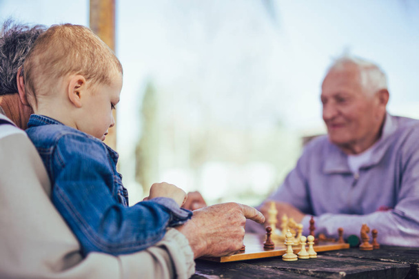 Pensionati attivi, vecchi amici e tempo libero, due anziani che si divertono e giocano a scacchi al parco, trascorrono del tempo con il nipote
 - Foto, immagini