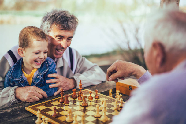 Pessoas aposentadas ativas, velhos amigos e tempo livre, dois homens seniores se divertindo e jogando xadrez no parque, passar tempo com o neto
 - Foto, Imagem