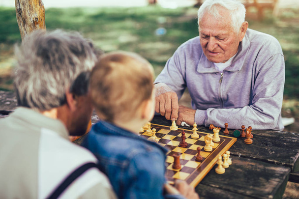 Aktywnych osób na emeryturze, starych znajomych i wolnego czasu, dwóch starszych mężczyzn dobra zabawa i gra w szachy w parku, spędzić czas z wnukiem - Zdjęcie, obraz