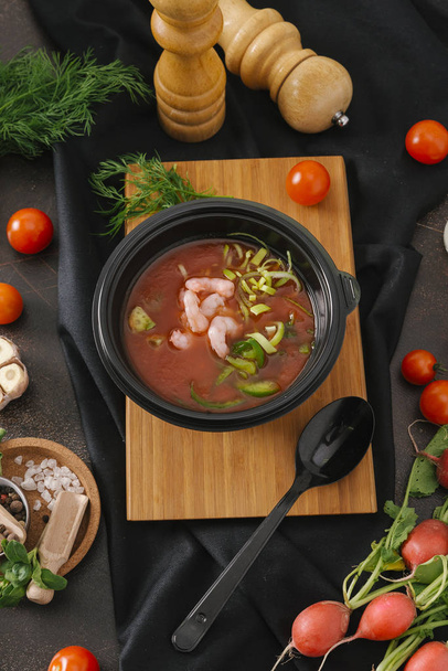 Složení potravin krevety polévka s rajčaty a avokádem v černém misku na dřevěné desce s zeleninou a nádobí - Fotografie, Obrázek