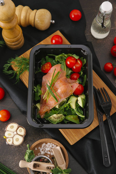 Salaatti lohta, kirsikkatomaatteja ja arugula mustalla tarjottimella pöydällä vihanneksia ja keittiötarvikkeita
 - Valokuva, kuva