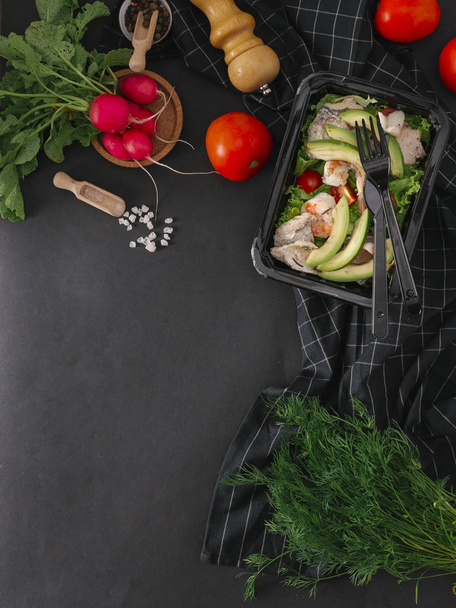 Food composition of salad with fish, shrimps, calamari, avocado, tomatoes and lettuce in black tray - Photo, Image