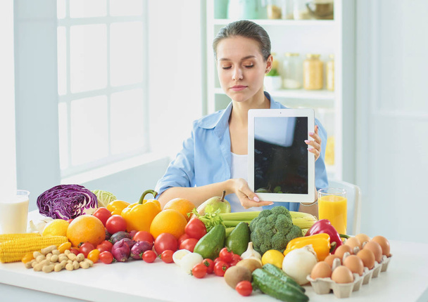 счастливая молодая домохозяйка сидит на кухне, готовя еду из кучи разнообразных свежих органических фруктов и овощей, избирательный фокус
 - Фото, изображение