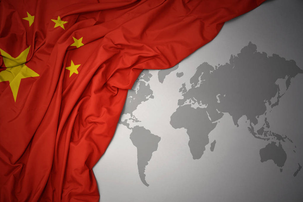 macha kolorowe flagi narodowej Chin na tle szarym świecie mapy. - Zdjęcie, obraz