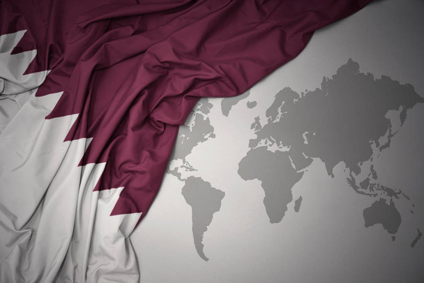 махаючи барвистим національним прапором Катару на сірому фоні карти світу
. - Фото, зображення