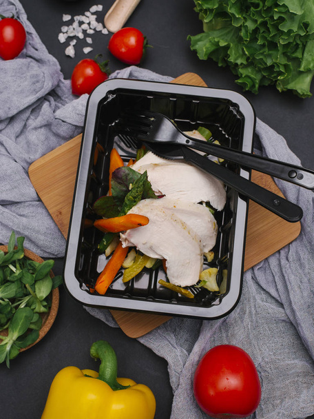 in Scheiben geschnittenes Hühnerfilet mit Gemüse in schwarzer Schale mit Messer und Gabel - Foto, Bild
