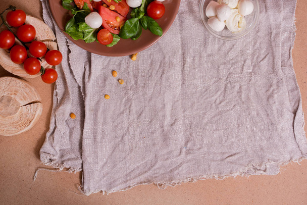 Summer fresh salad from tomatoes, cabbage, basil on a linen napkin, vintage village style wabi sabi. Preparation of healthy food. The arrangement is square. Copy space, top view - Фото, изображение