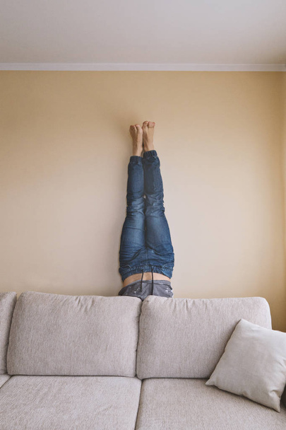 Man handstanding behind couch, yoga and spring cleaning concept, furniture care - Photo, image