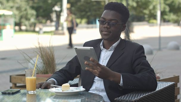 Handsome afro american man is using a tablet, while sitting in outside cafe - Valokuva, kuva