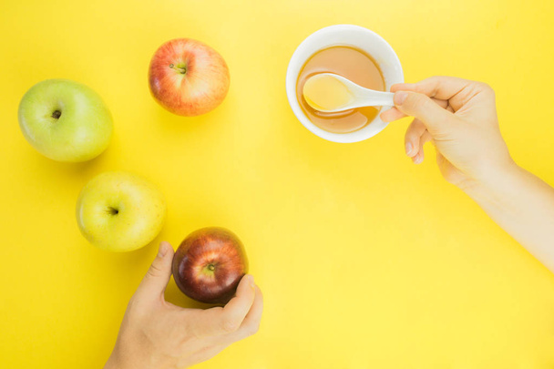 謹賀新年、リンゴ、黄色の背景の上に蜂蜜のカップ。手に蜂蜜とリンゴを到達します。. - 写真・画像
