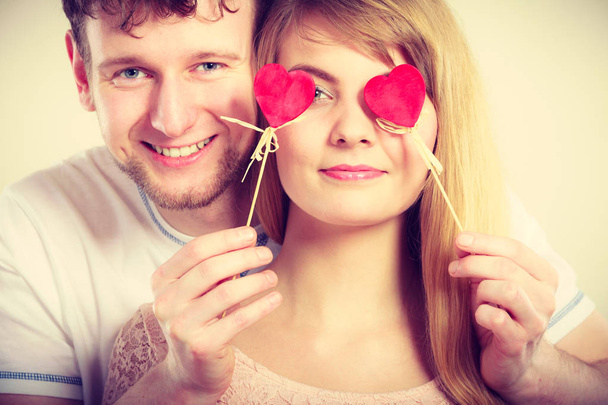 Love and happiness concept. Cheerful enjoyable young couple with little small hearts on sticks covering woman man eyes. Lovers blinded by their big love. - Fotografie, Obrázek