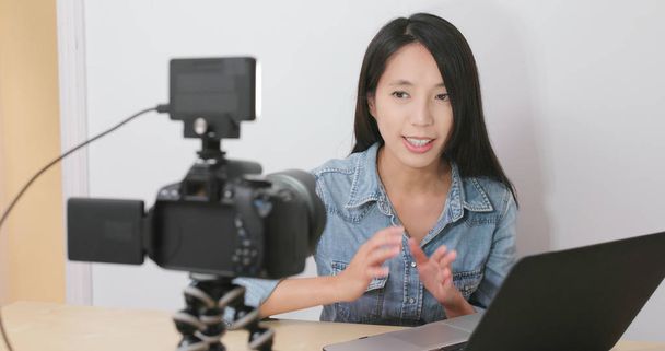 Γυναίκα μιλώντας μπροστά από την ψηφιακή φωτογραφική μηχανή με το φορητό υπολογιστή για την πραγματοποίηση vlog στο σπίτι  - Φωτογραφία, εικόνα