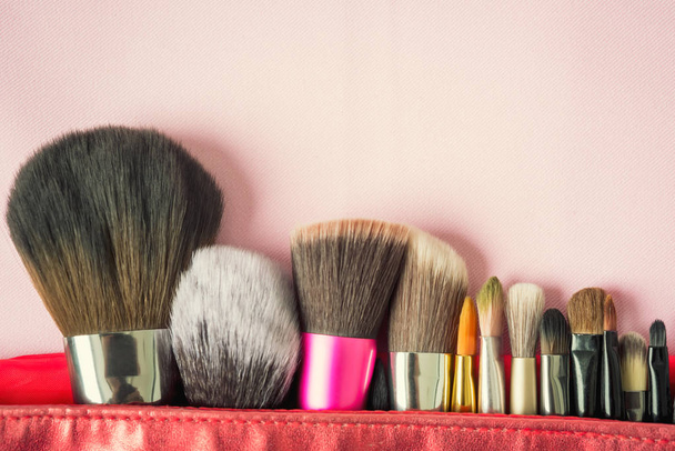 Muchos cepillo de moda para maquillaje o cosméticos en bolsa roja sobre fondo rosa borroso. Visión de belleza y diseño. Filtrado retro y vintage
. - Foto, imagen