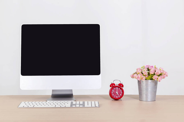 Tietokone, joka näyttää tyhjän näytön työpöydällä punaisella kellolla ja kukkaruukulla
. - Valokuva, kuva