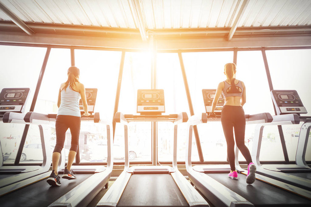 Sport girls running on treadmill in fitness gym at sunrise. - Photo, Image