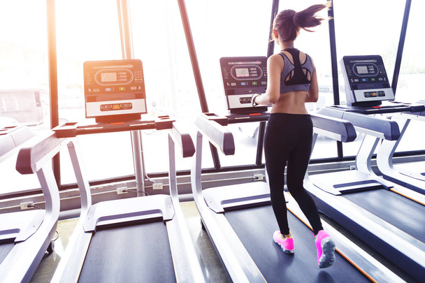 Young sport woman running on electric treadmill in gym at sunrise in the morning. - Photo, Image