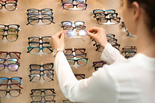 Female ophthalmologist taking glasses from showcase in optical store - Valokuva, kuva