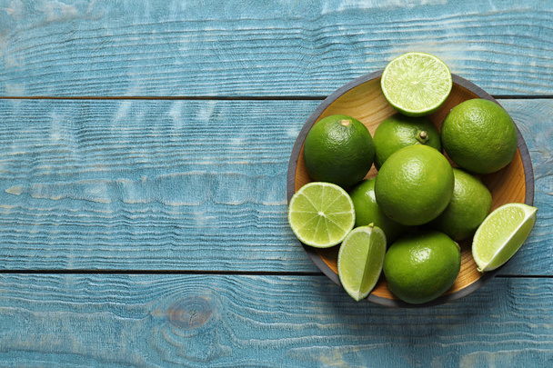 Bowl with fresh ripe limes on wooden background, top view - Фото, изображение