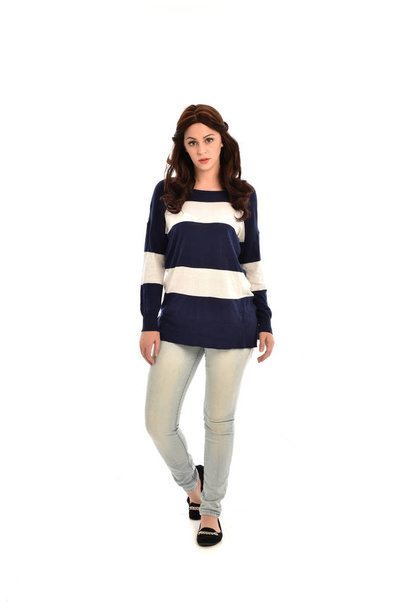 full length portrait of girl wearing striped blue and white jumper and jeans. standing pose on white studio background. - Fotó, kép