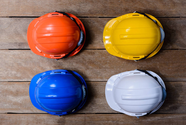 Yellow, Orange, White and Blue protective safety helmet on old wooden background. safety first concepts - Foto, imagen