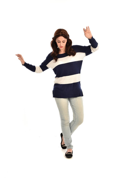 портрет девушки в полосатом сине-белом свитере и джинсах. стоячая поза на белом студийном фоне
. - Фото, изображение
