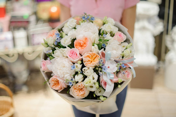 Woman holding a large bouquet in tender tones consisting of peonies, roses and other flowers in a flower shop - Foto, Imagem