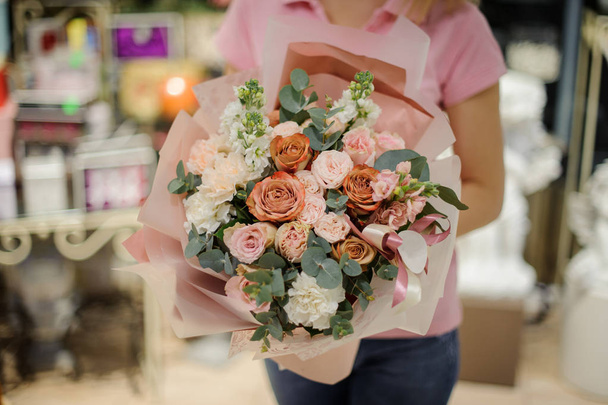 Woman holding a stylish flower composition in golden and pink tones consisting of roses and eucalyptus in a flower shop - Фото, изображение