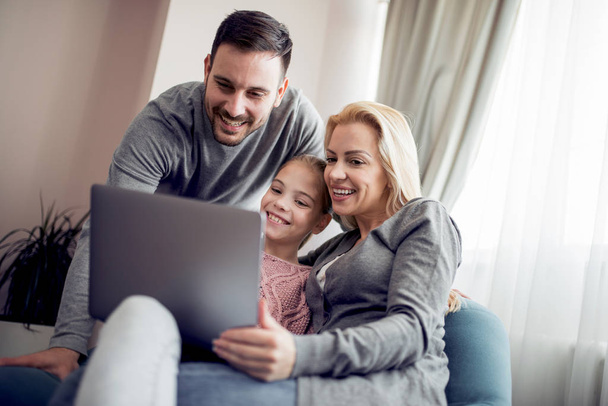 Parents heureux avec fille en utilisant un ordinateur portable dans le salon
. - Photo, image
