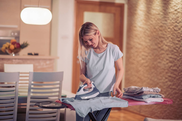 Красивая молодая женщина гладит одежду дома
. - Фото, изображение
