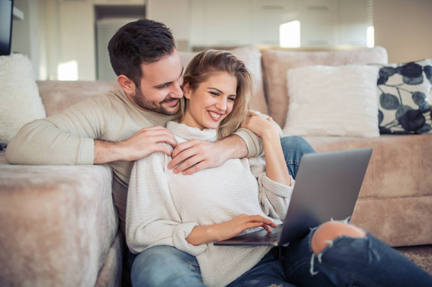 Happy νεαρό ζευγάρι χαλαρώνετε στο σπίτι, χρησιμοποιώντας το laptop μαζί. - Φωτογραφία, εικόνα