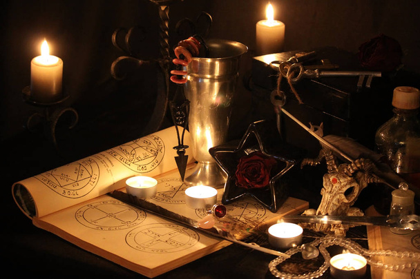 Černá magie kouzla. Wiccan kouzla a byliny. Stále Live: Staré olejové lampy, starožitné knihy, sušené růže poupata, hořící svíčka v měděnou mísu, lékovky, levandule, Pulsatilla pratensis na starožitný pozadí. Wicca pozadí. - Fotografie, Obrázek