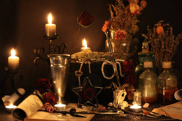 Black Magic Spells. Wiccan spells and herbs. Still Live: Old oil lamps, antique books, dried rose buds, a burning candle in a copper bowl, medicine bottles, lavender, Pulsatilla pratensis on an antique background. Wicca background. - Photo, Image