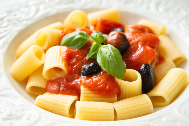 Maccheroni con salsa de tomate, aceitunas y hojas de albahaca fresca
 - Foto, imagen