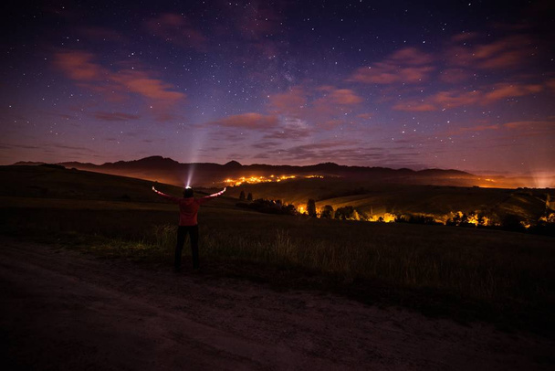 Jeune femme heureuse à la nuit étoilée dans les montagnes. Pointant une lampe torche vers le ciel. Concept de liberté et détente
 - Photo, image