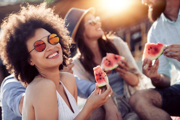 Jovens amigos alegres comendo melancia na praia, se divertindo juntos
. - Foto, Imagem